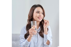 Image A woman taking a supplement while holding a glass of water.