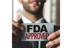 Image A man wearing a black and white and a five-o-clock shadow style beard holds a card in front of him that says, "FDA approved."