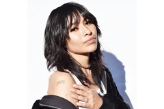 A woman with a wolf haircut holding her shoulder.