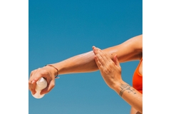 A hand applying sunscreen on her arm.