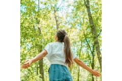 woman spreads arms open looking up at trees