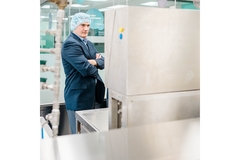 Image A man in a blue suit wearing a safety cap and standing inside a beverage production plant.