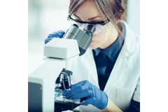 Image Researcher in a lab coat looking through a microscope.