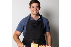 Image A man in a blue shirt and black apron smiling.