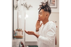 A man looking in the mirror and applying cream to his face.