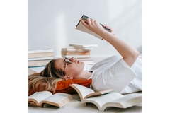 A girl lies in a pile of books reading books.