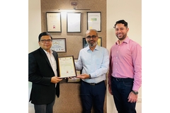 Three men in formal clothes with two of them holding a framed certificate in their hands.