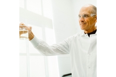 Image An old bald man smiling and holding a flask with oil.