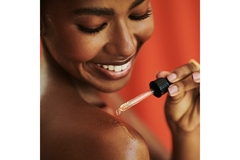 Image A woman smiling and putting a dropper of serum on her shoulder.