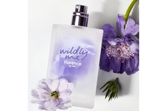 Wildly Me perfume from Florence by Mills in front of a purple flower.
