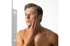 Image A man touching his face and looking in the mirror.