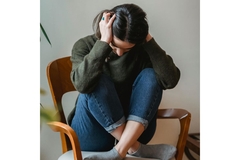 Image A woman suffering from migraines, sitting on a chair with her hands in her hair.