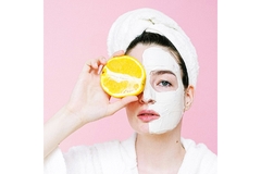 Woman wearing skin care mask holds an orange