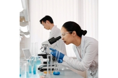 A woman looks through a microscope in a lab.