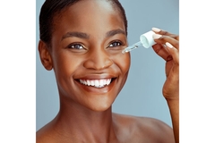 Woman with clear skin applies product to cheek using dropper