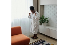 Image Woman in a bathrobe, standing on a weight scale and looking happy.
