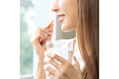 Image Girl takes a pill while looking out of a sunlit window.