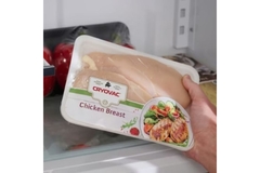 Image Hand holding chicken breast in wrapped food tray.