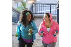 Two women exercising outside, walking up stairs with weights in their hands.