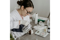 Image A woman wearing a lab coat pouring a mixture into a beaker.