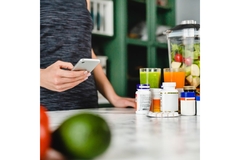 Image Woman looks at phone, supplement bottles next to her.