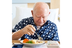 Senior man patient in hospital bed eating plant-base protein for liver health.