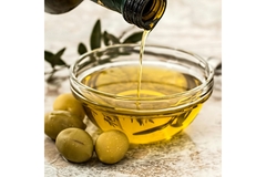 Image A hand pouring olive oil into a glass bowl from a bottle.