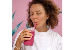 Image A woman sipping a pink smoothie from a straw in a glass.