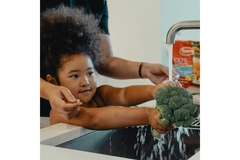 Image A girl washes broccoli in the sink.