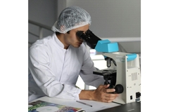 Image Researcher in a lab coat looking through a microscope.