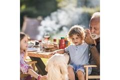 Image Grandfather and two children eating a picnic outside in the summer.