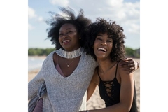 Image Two African women hugging and laughing on the beach.
