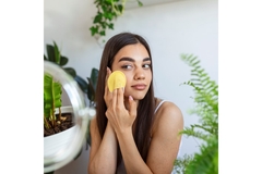 Image A woman using a cotton pad on her face while surrounded by plants.
