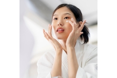 A woman looking in the mirror and putting on eye cream.