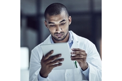 Researcher in a lab coat looking on a tablet.
