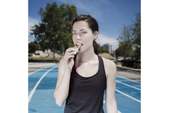 Image A woman eats a bar on running track.