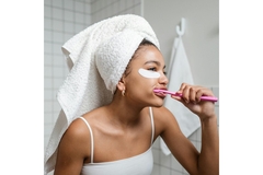 A woman brushing her teeth with a towel on her head.