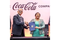 People shaking hands in front of Coca-Cola banner.