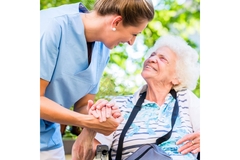 Nurse holding hand of senior person in a wheelchair.