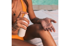 Image A woman in a one-piece spraying her hand with sunscreen.