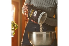 Image A baker's hand pouring flour in a container.