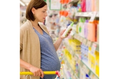 Image Pregnant woman looks at product label while shopping down aisle