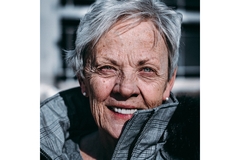 An older woman smiling a warm, sliver, puffy coat.
