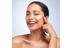 Image smiling woman with clear skin applies moisturizer on cheek