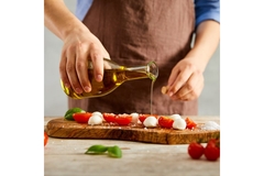 Image Person pooring olive oil over tomatoes and mozzarella.