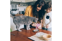 A woman and a child feed a cat treats on their dinner table.
