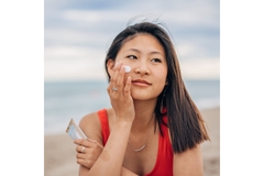 A woman putting sunscreen on her cheek at the beach.