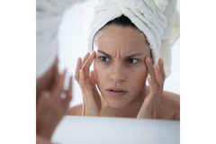 worried woman looks in mirror at face