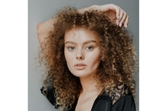 A woman with curly hair and her arm over her head.