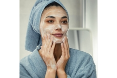 woman in robe washes face looking at mirror